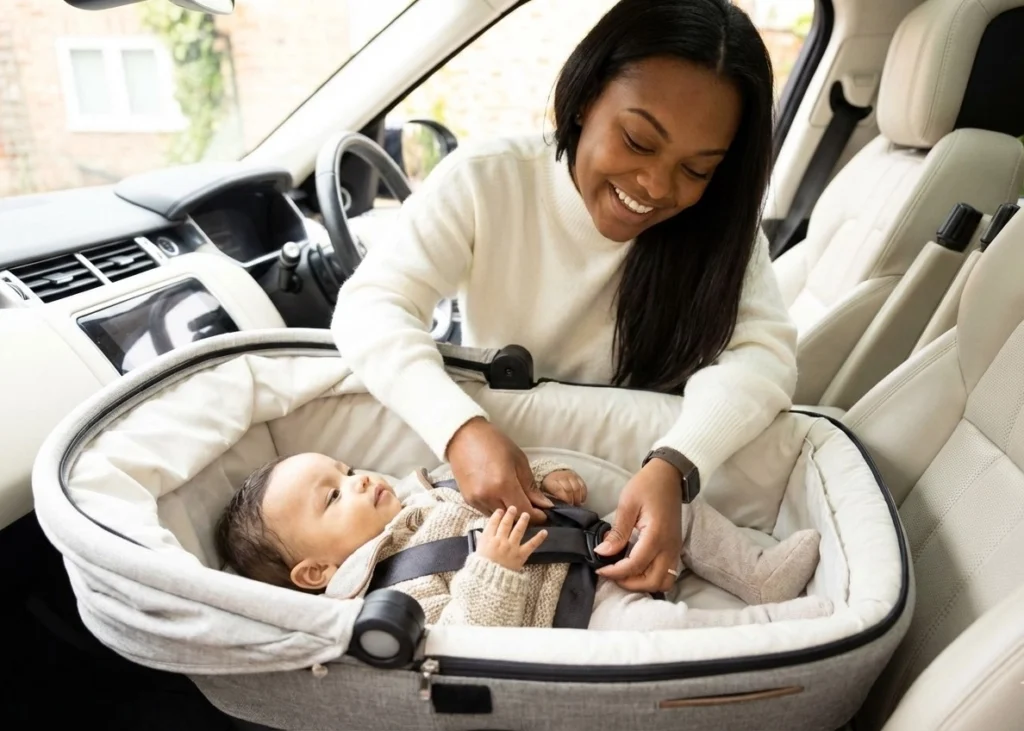 Realistic photo of a smiling mother fastening her baby into a rear-facing safety seat, demonstrating proper adherence to Alabama Car Seat Laws.