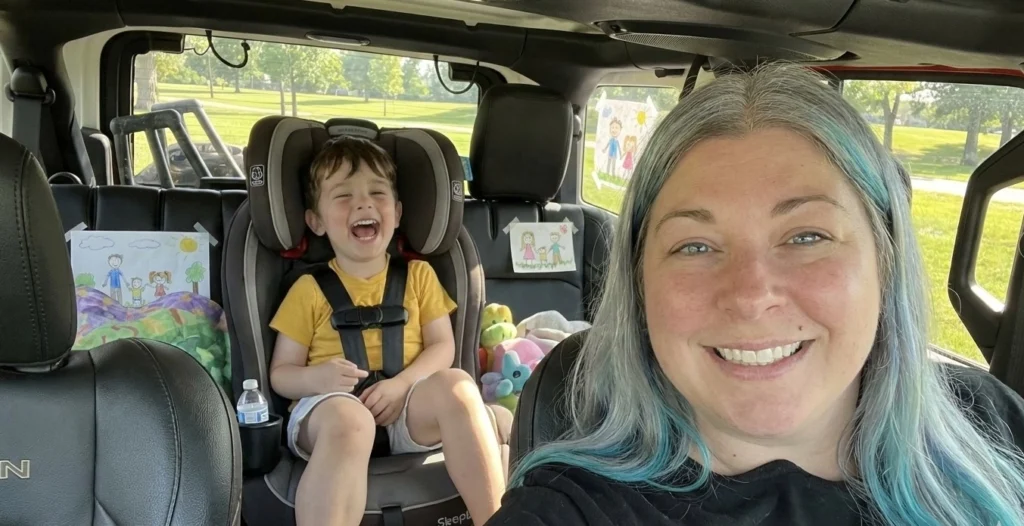 Realistic illustration of a happy mother and child in a vehicle, showing the toddler secured in a safety seat in compliance with Alabama Car Seat Laws.